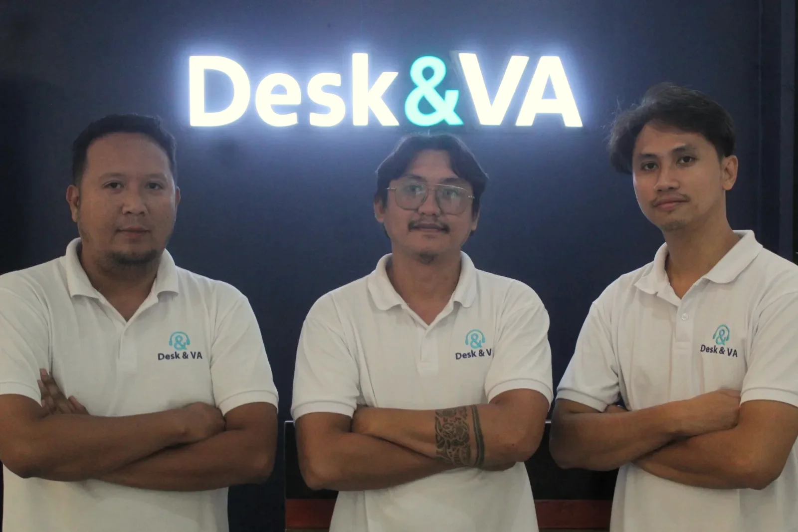 Three Desk & VA team members in front of the illuminated Desk & VA sign